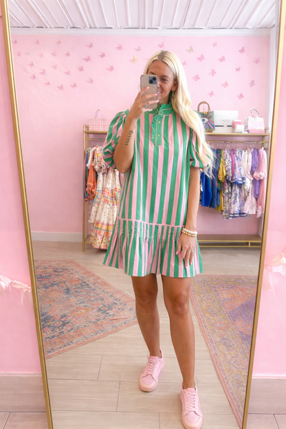 Person wearing a green and white striped dress in a store with pink walls.