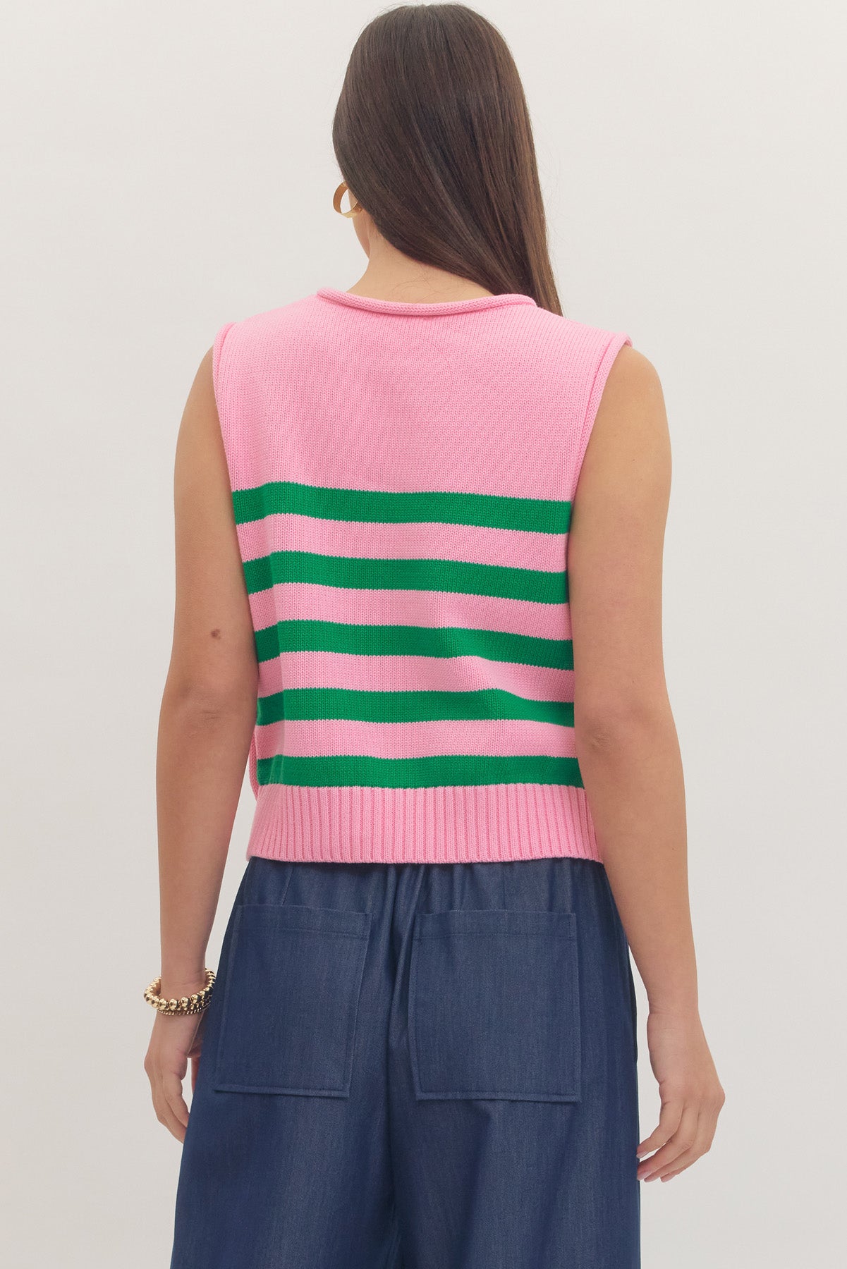 Person wearing a pink sleeveless top with green stripes and blue pants on a plain background