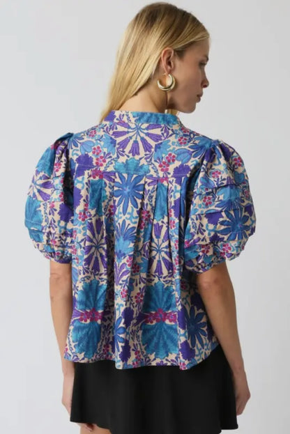 Back view of the blue and violet floral puff sleeve blouse showing pleated details and bold embroidered-style pattern from Milo & Lily Boutique.