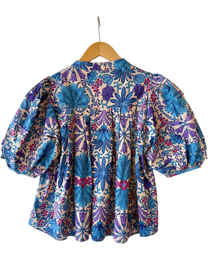 Back view of blue and purple floral blouse on hanger showing flowy silhouette and puff sleeve detail from Milo & Lily Boutique.