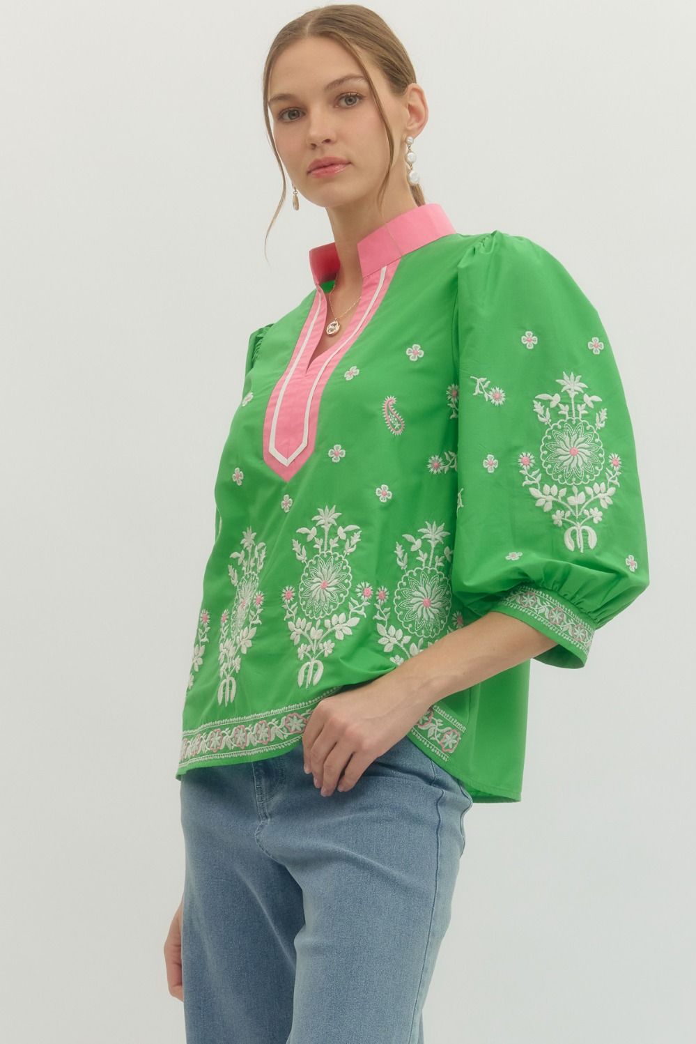 Woman wearing a green embroidered blouse with pink trim on a white background