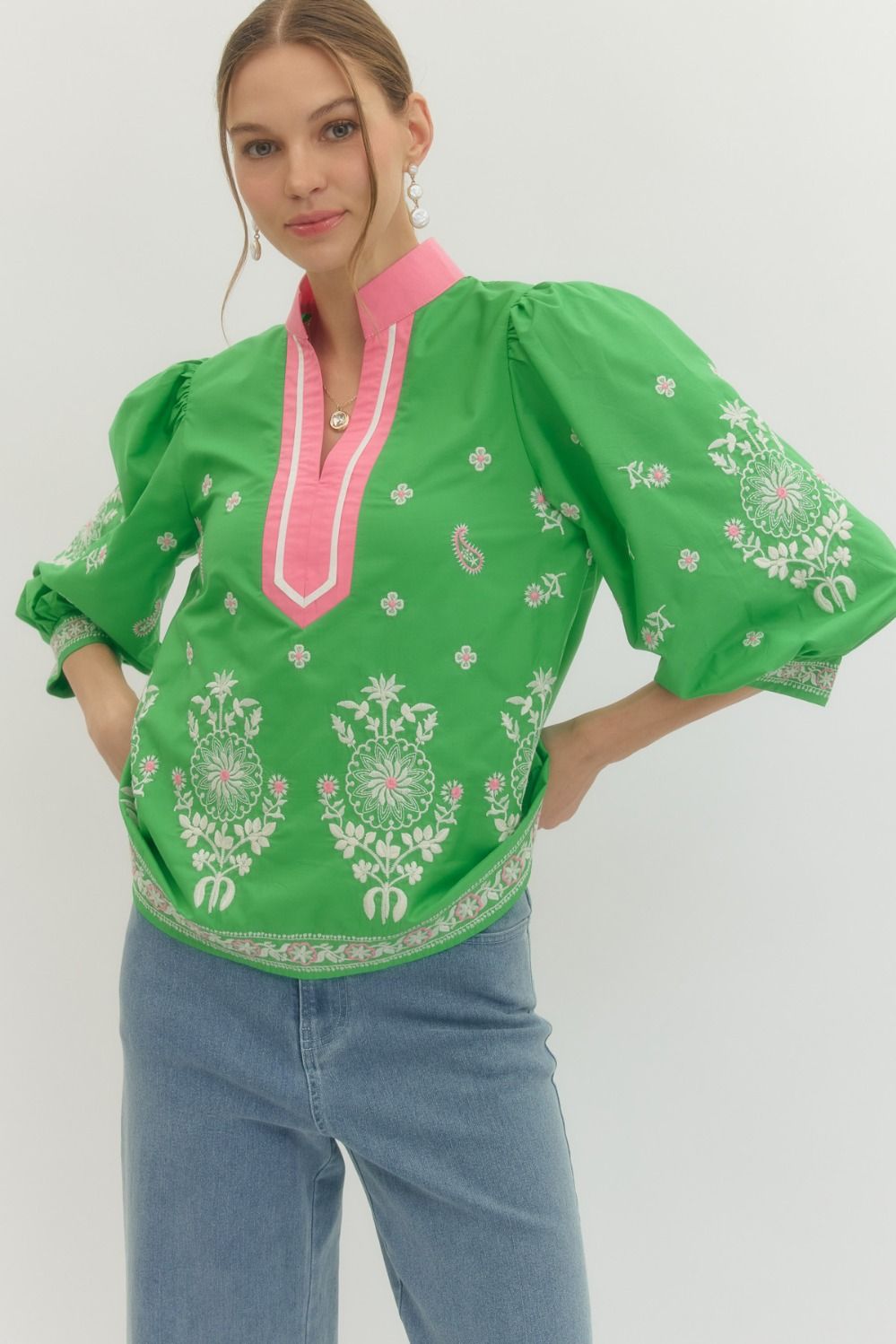 Woman wearing a green blouse with floral patterns and pink accents on a white background