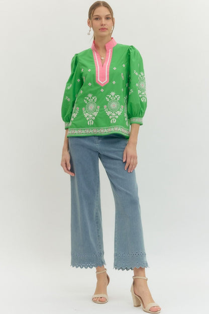 Woman wearing a green embroidered top and blue pants on a white background