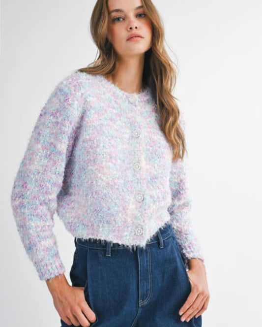Model wearing The Frosted Sugar Knit — a pastel fuzzy cardigan with crystal buttons in shades of lilac, blue, and pink paired with high-rise jeans.