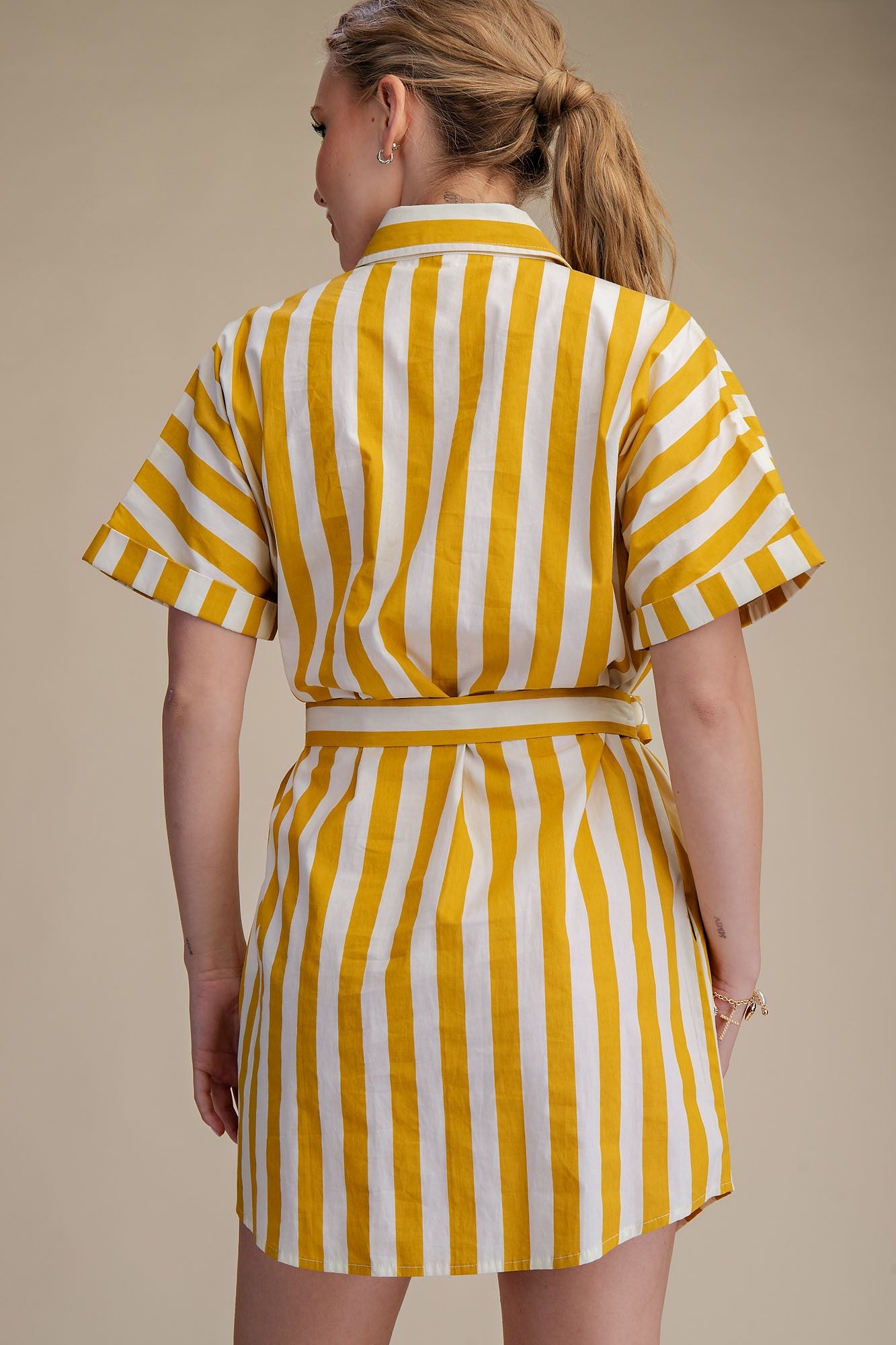 Woman wearing a yellow and white striped dress against a beige background