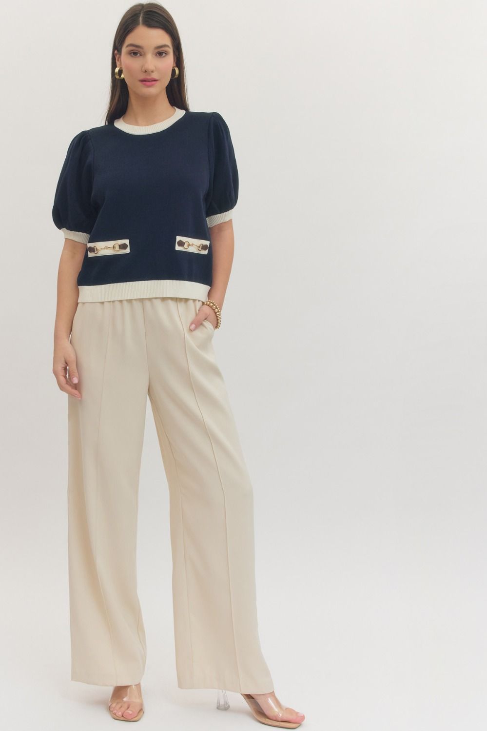 Woman wearing a navy sweater with white trim and beige pants on a white background