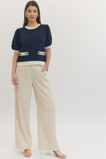 Woman wearing a navy sweater with white trim and beige pants on a white background
