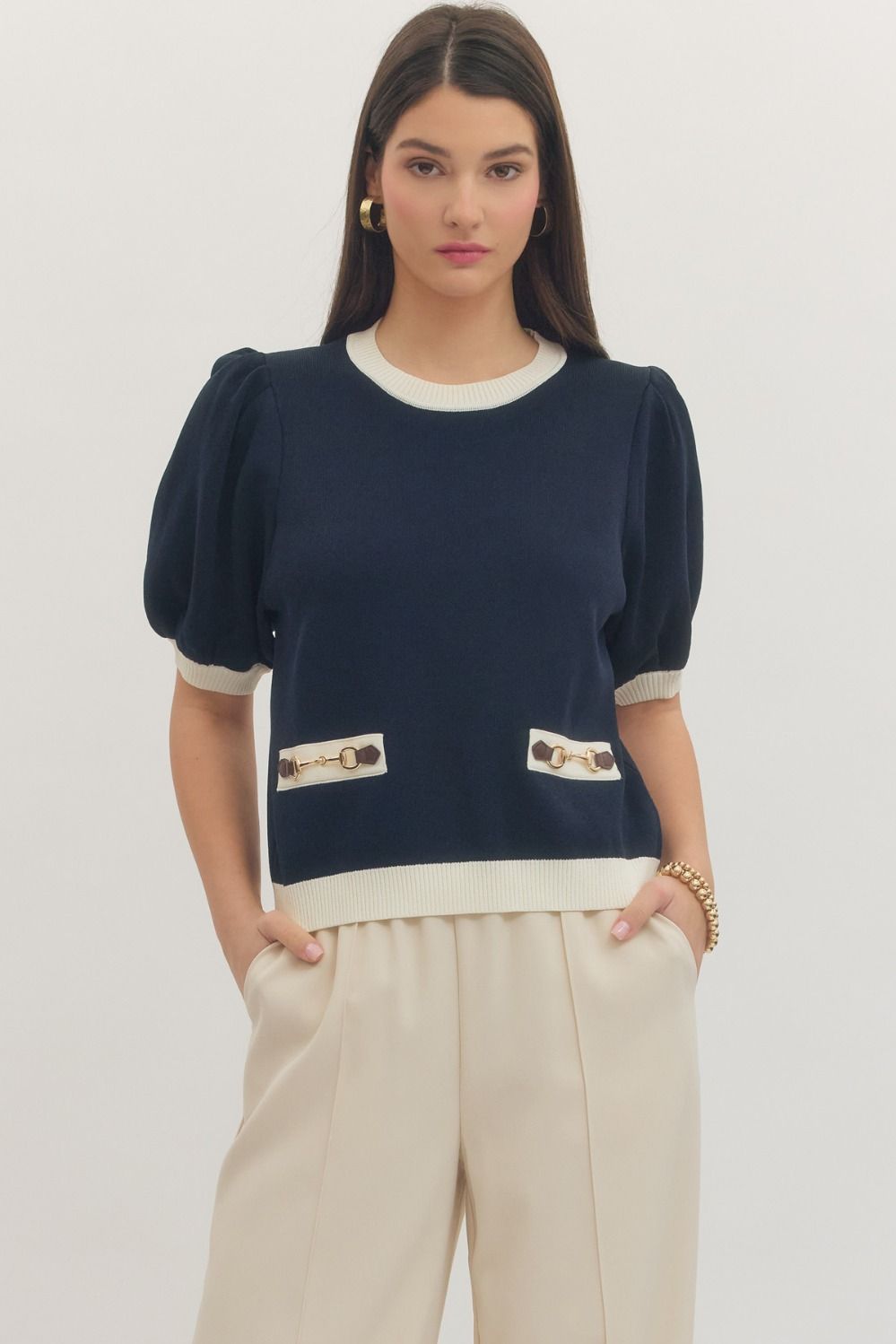 Woman wearing a navy blue top with white trim and beige pants on a plain background