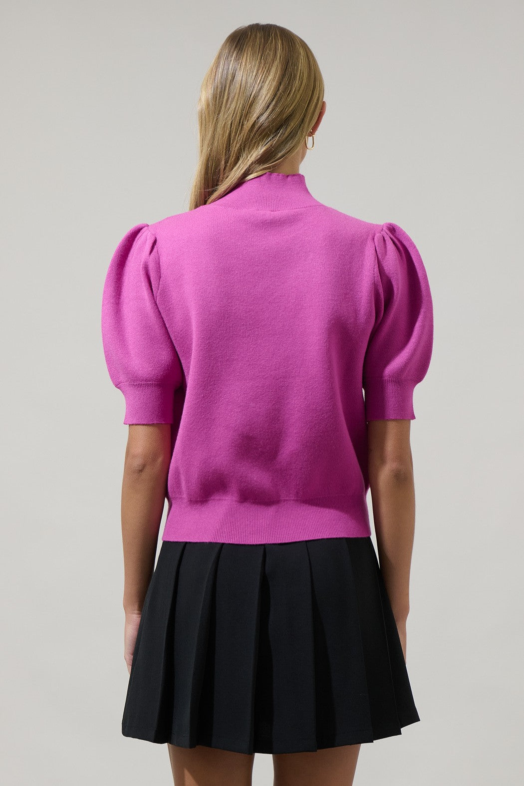Person wearing a pink top with puff sleeves and a black pleated skirt on a gray background