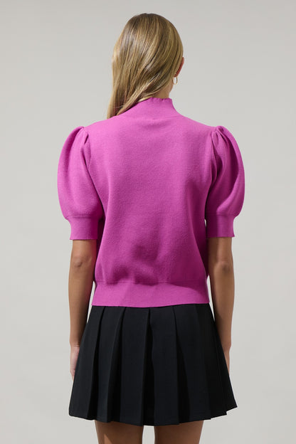 Person wearing a pink top with puff sleeves and a black pleated skirt on a gray background