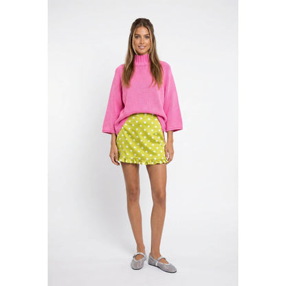 Full-length front view of hibiscus pink mock-neck batwing sweater styled with a lime polka-dot skirt.