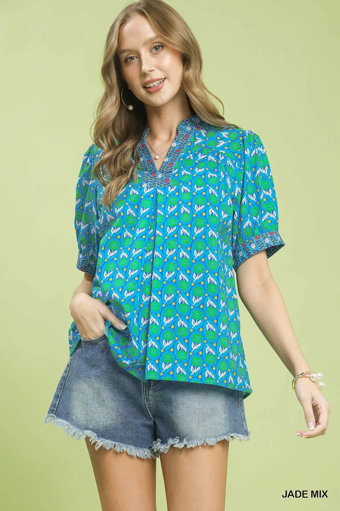 Woman wearing a blue and green patterned blouse with denim shorts on a light green background