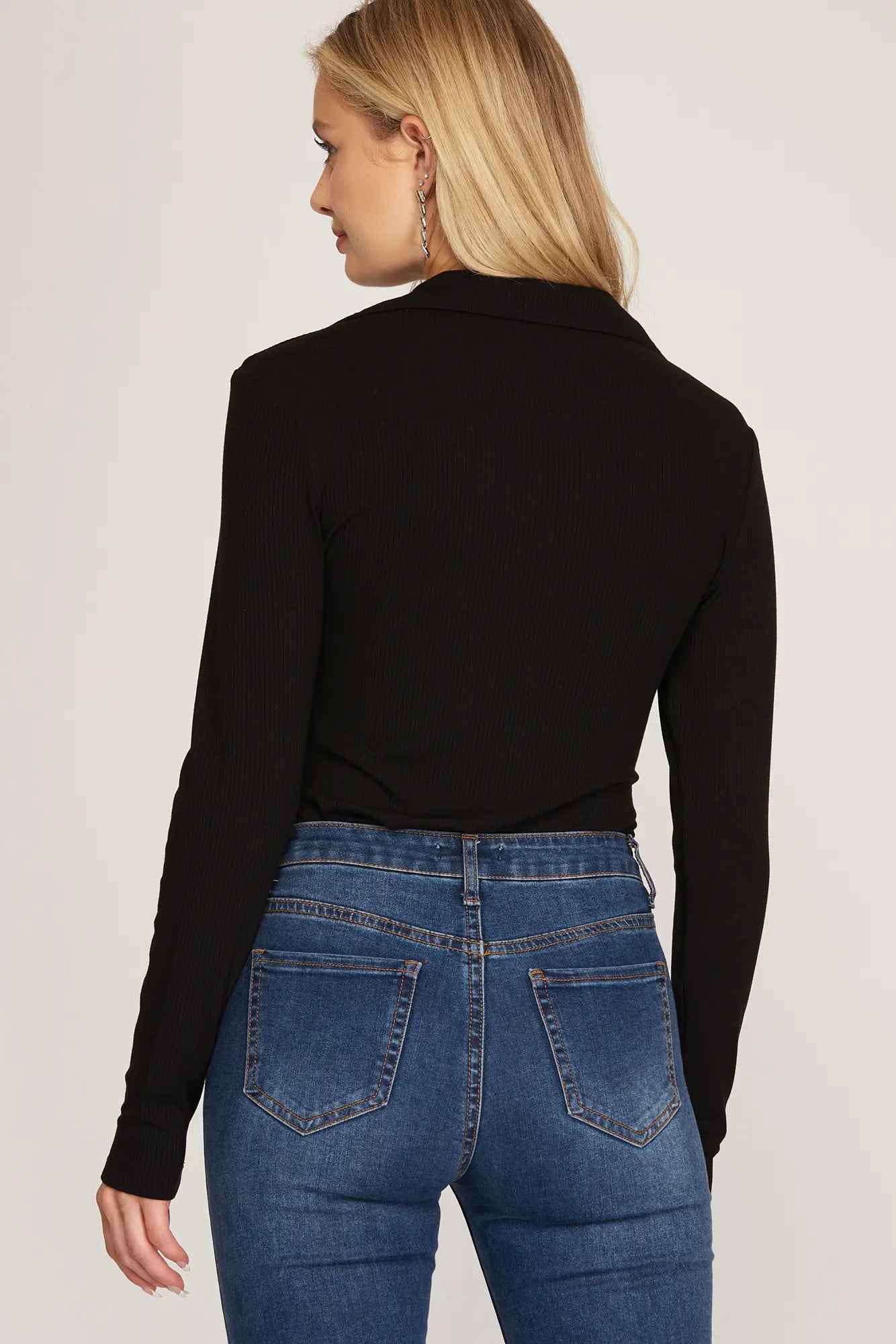 Person wearing a black long-sleeve top and blue jeans on a plain background