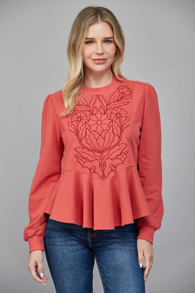 Front view of coral embroidered peplum top with long sleeves