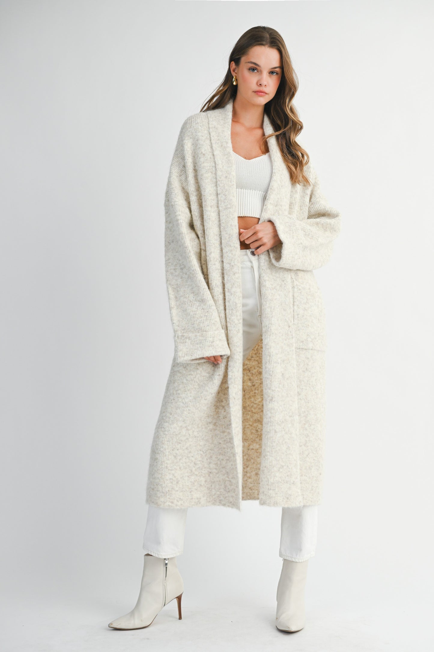 Front view of long oatmeal knit cardigan styled with white outfit and boots