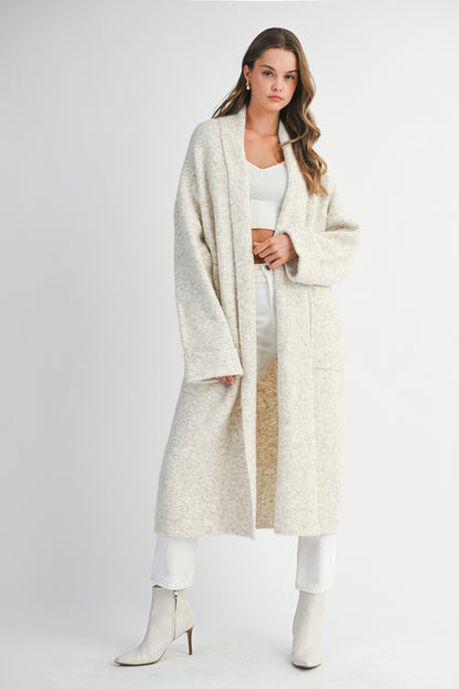 Front view of long oatmeal knit cardigan styled with white outfit and boots