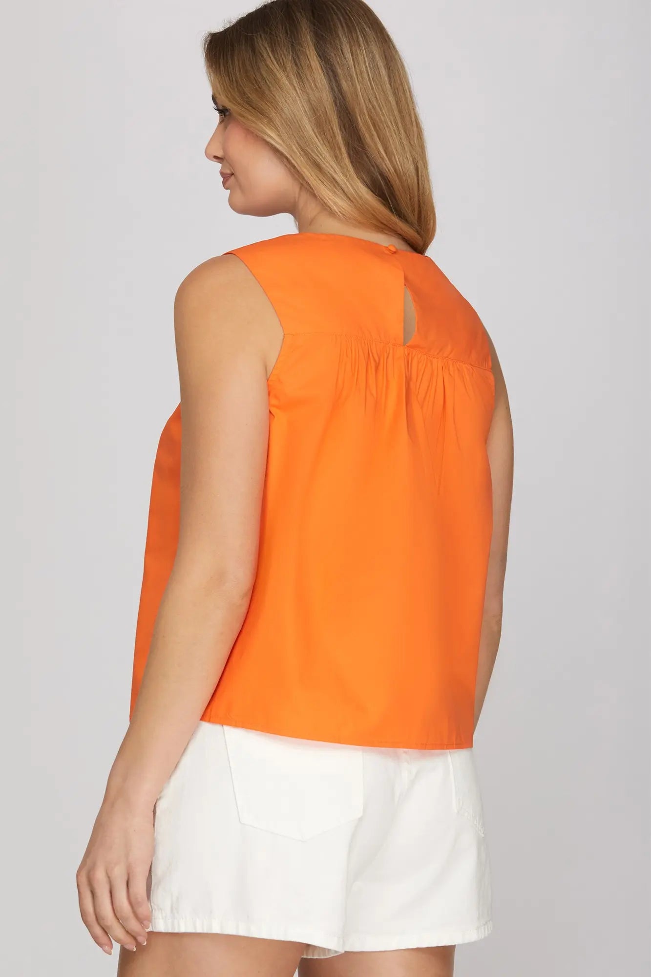 Woman wearing an orange sleeveless top and white skirt on a plain background