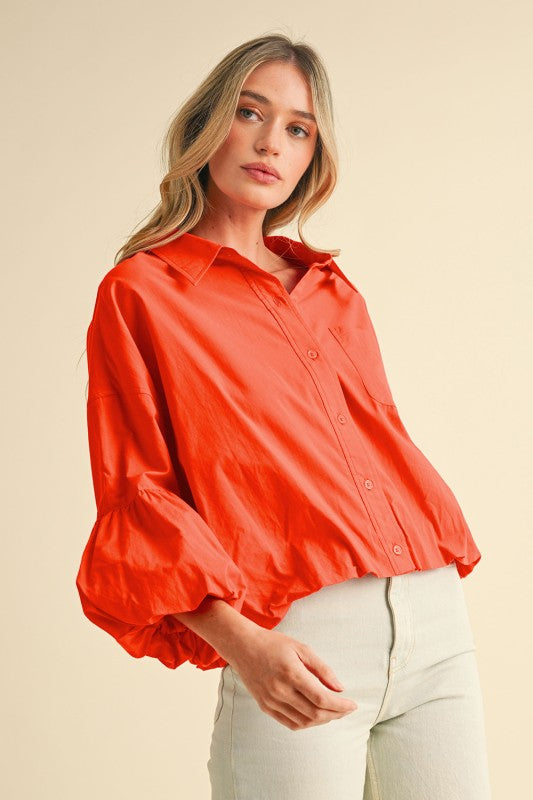 Side view of bright orange collared button-down blouse with dramatic puff sleeves and chest pocket.