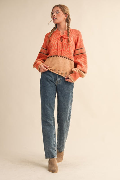 Full-length view of orange tie-neck patterned sweater styled with jeans and boots.