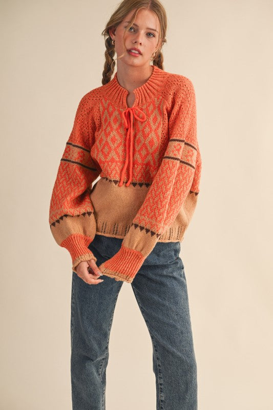 Model wearing orange and camel patterned knit pullover sweater with blue denim jeans.