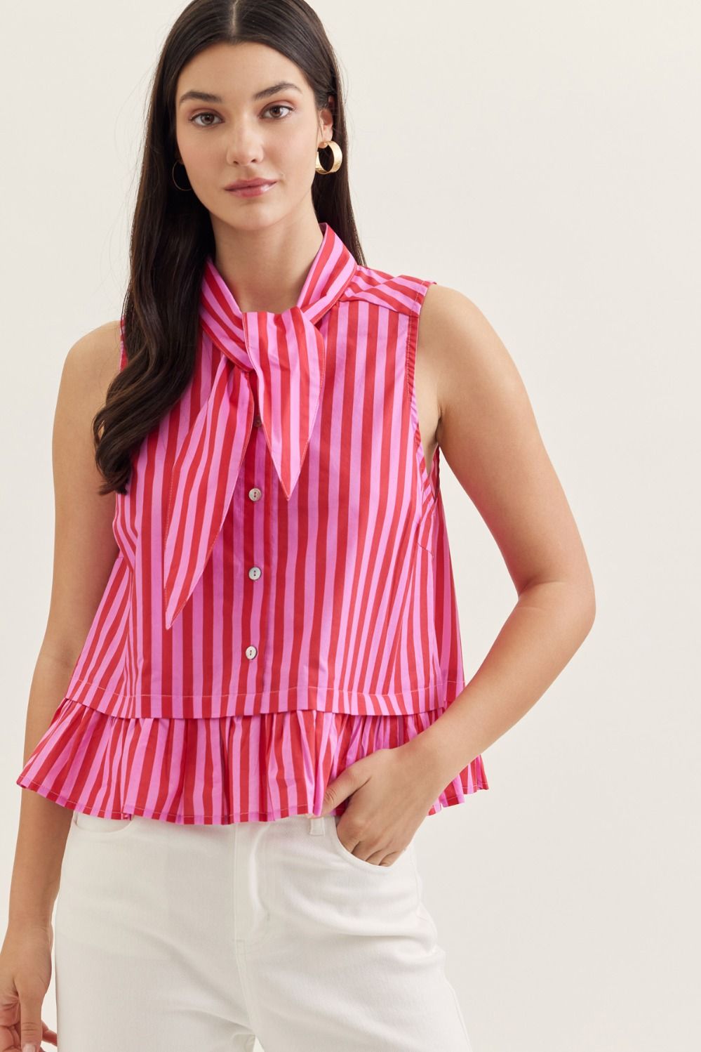 Woman wearing a pink and white striped sleeveless top with a tie detail on a plain background