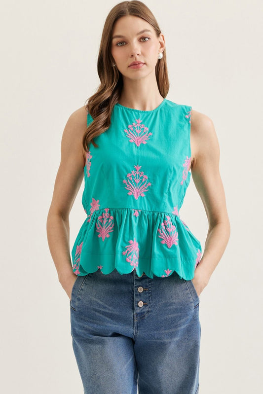 Woman wearing a teal top with pink floral patterns and blue jeans on a plain background