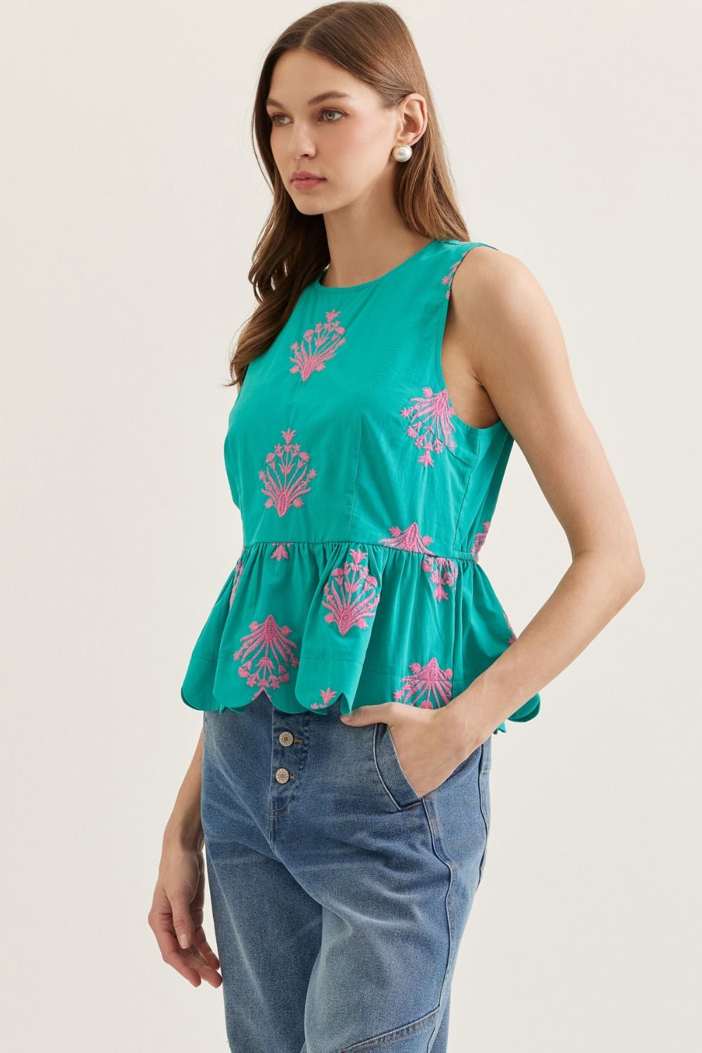 Woman wearing a teal top with pink floral patterns and blue jeans on a light background