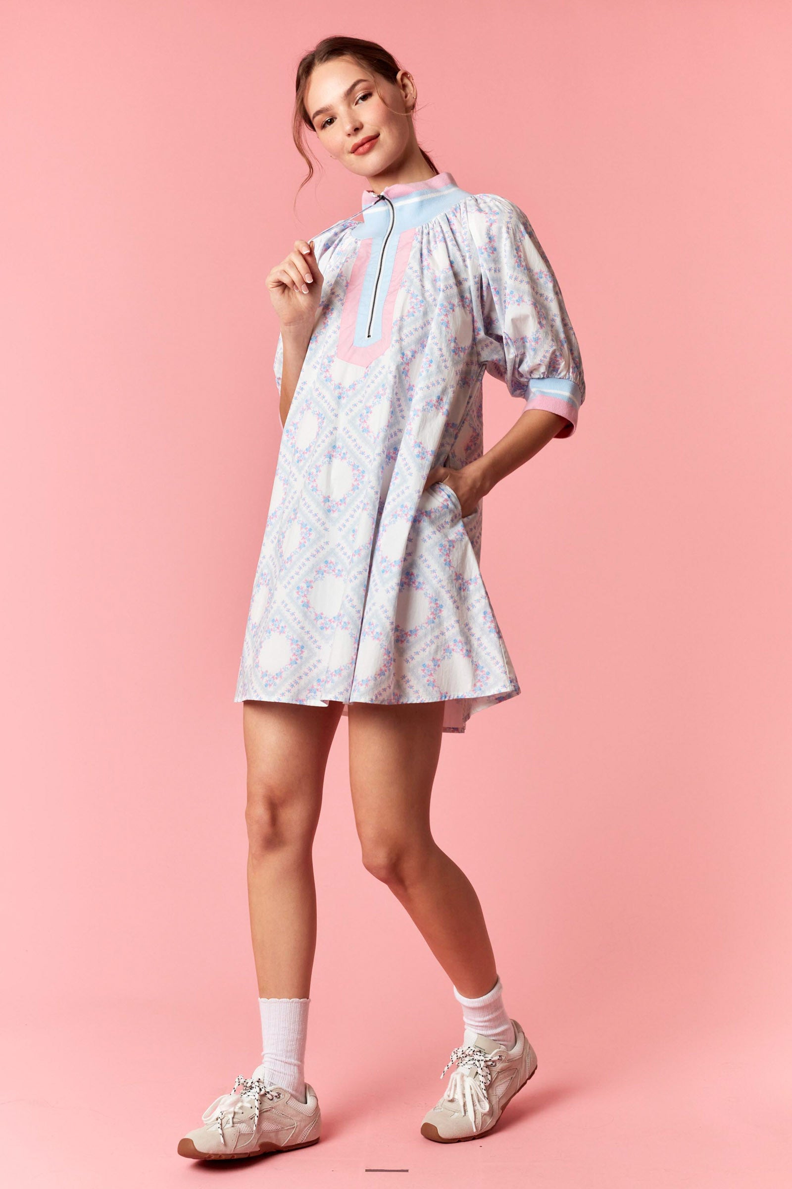 Woman wearing a light blue dress with a pink design on a pink background