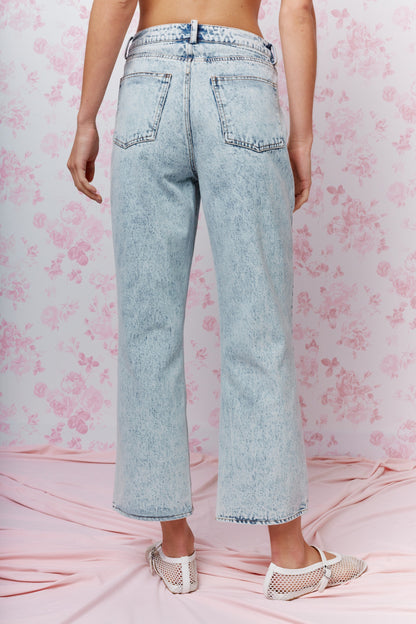 Person wearing light blue acid-wash jeans on a pink floral background