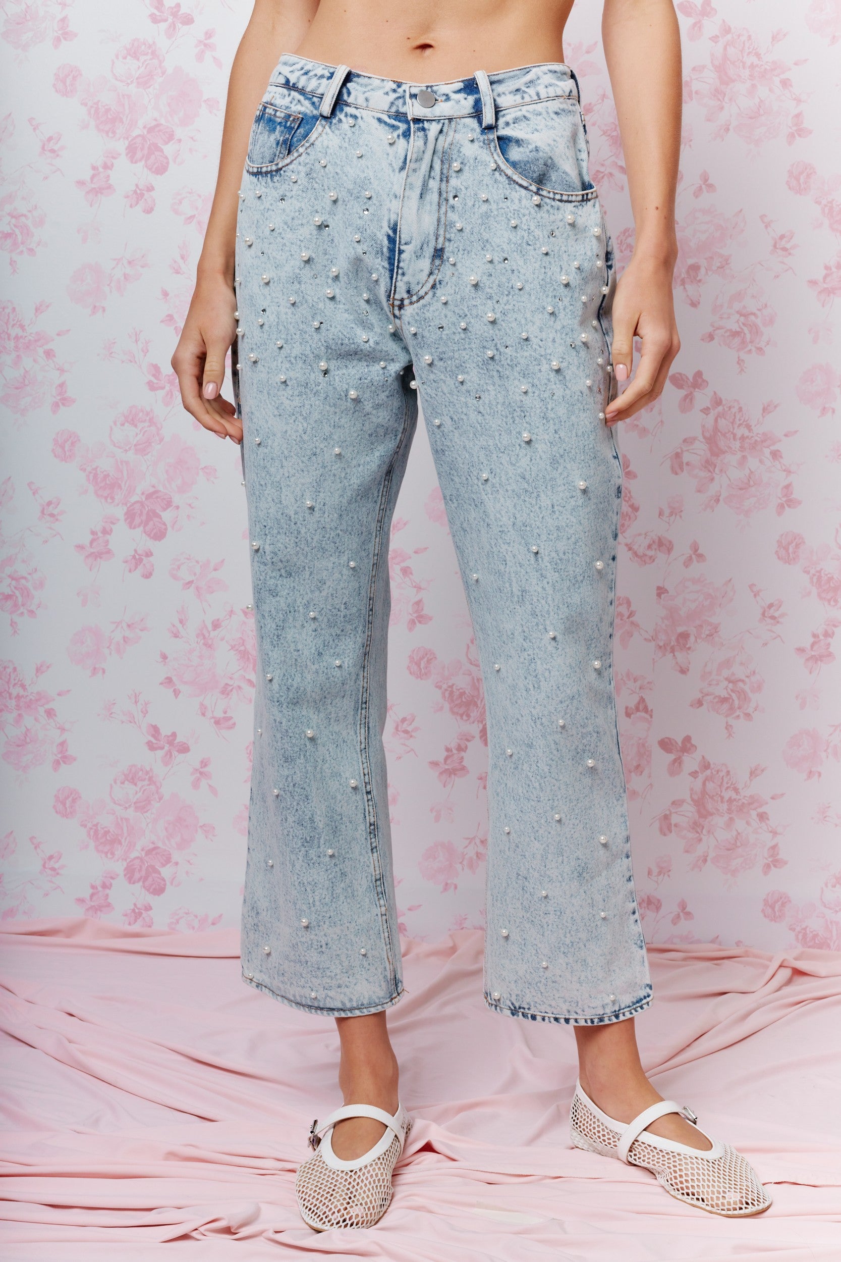 Light blue jeans with rhinestone embellishments on a pink floral background
