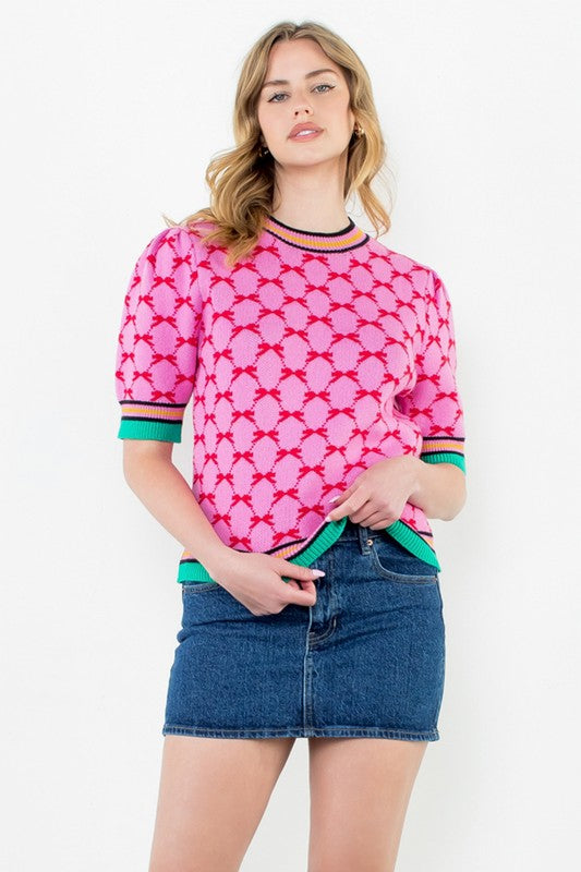 Model wearing a bright pink and red geometric knit top with puff sleeves and colorful striped trim — playful boutique sweater from Milo & Lily.
