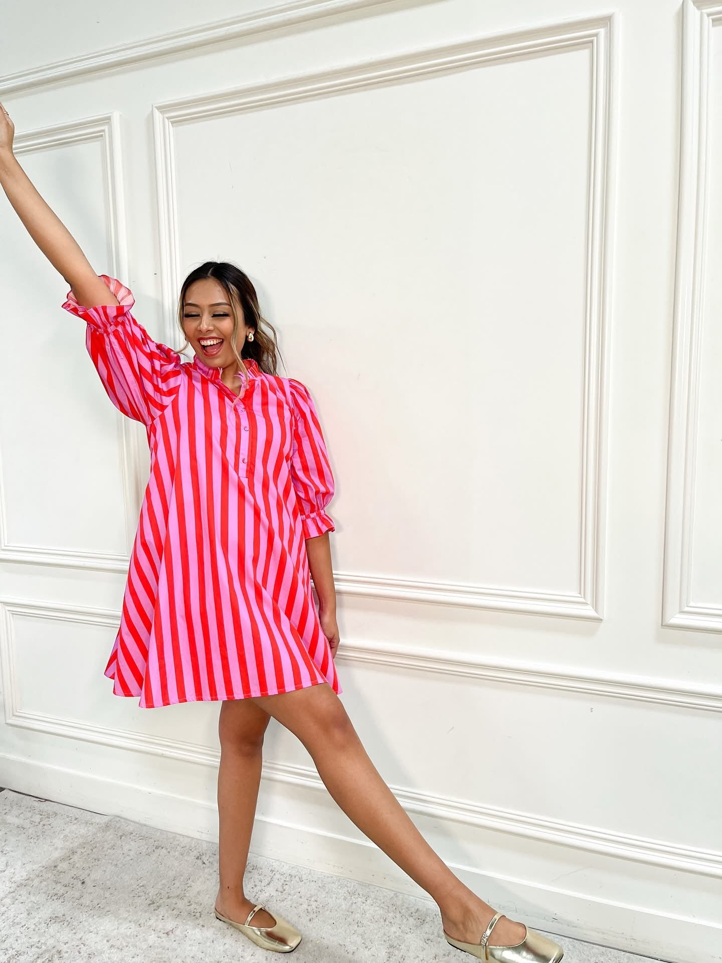 Woman wearing a red and white striped dress against a white paneled wall.