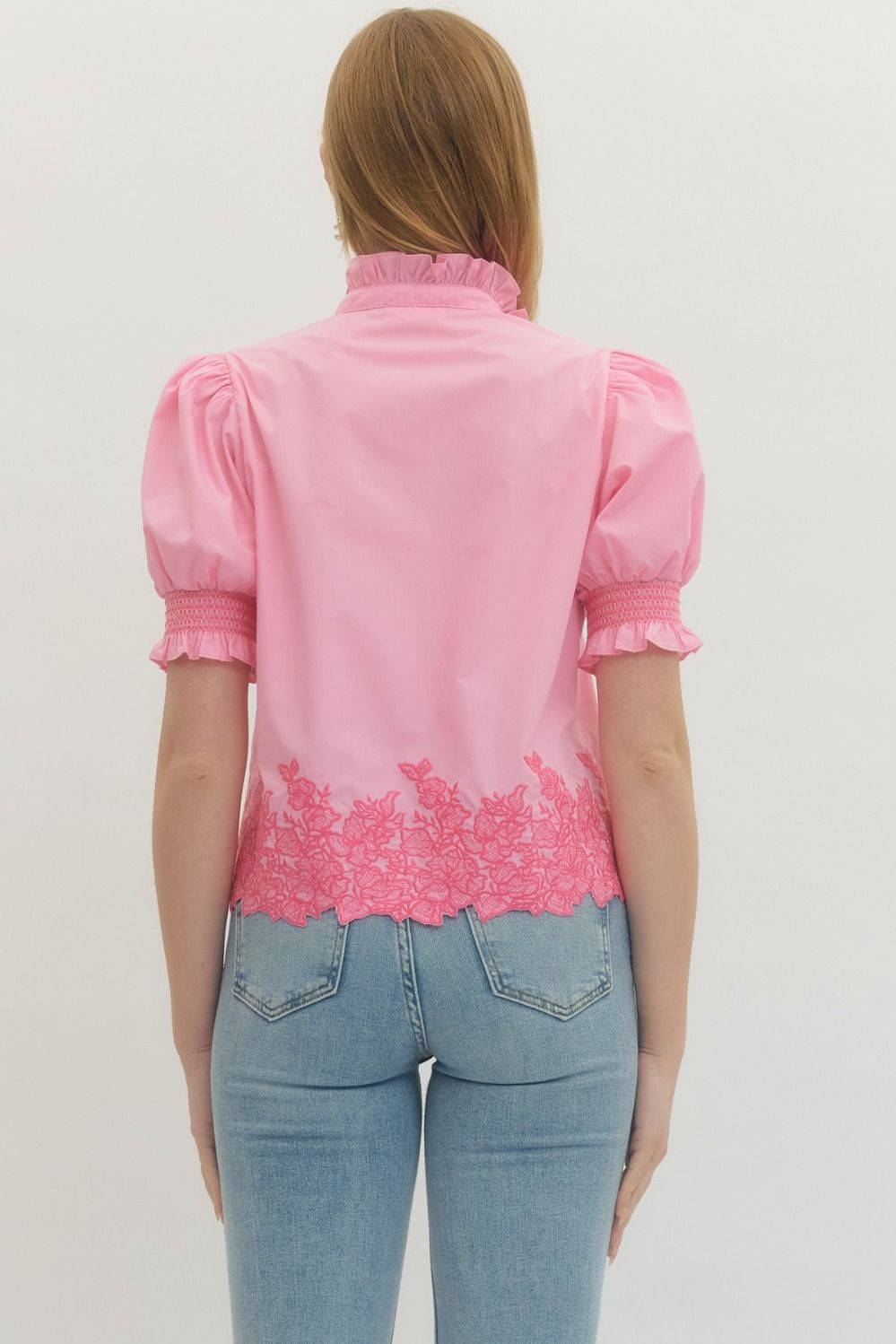 Person wearing a pink blouse with lace details and blue jeans on a light gray background