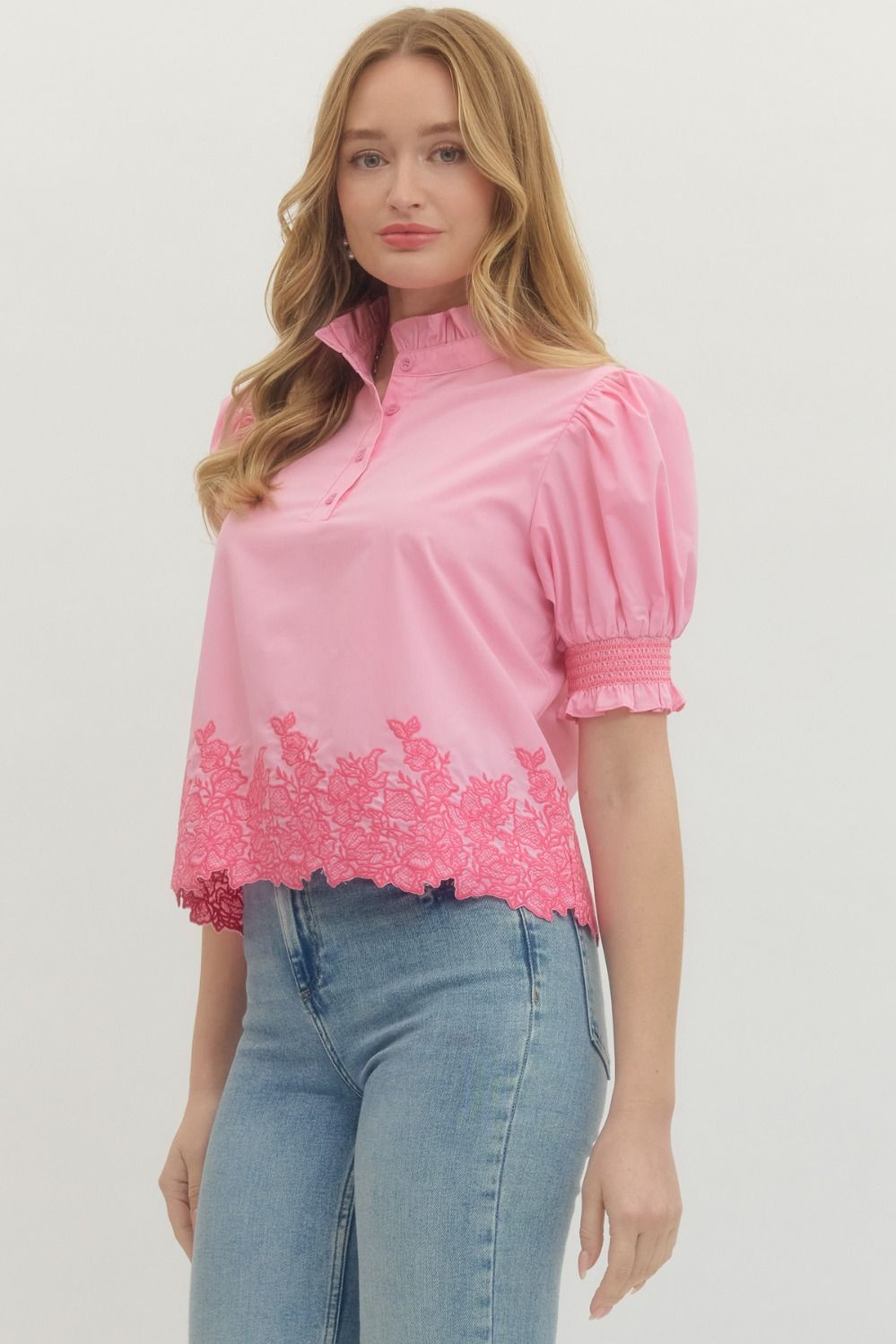 Woman wearing a pink blouse with lace details and blue jeans on a white background