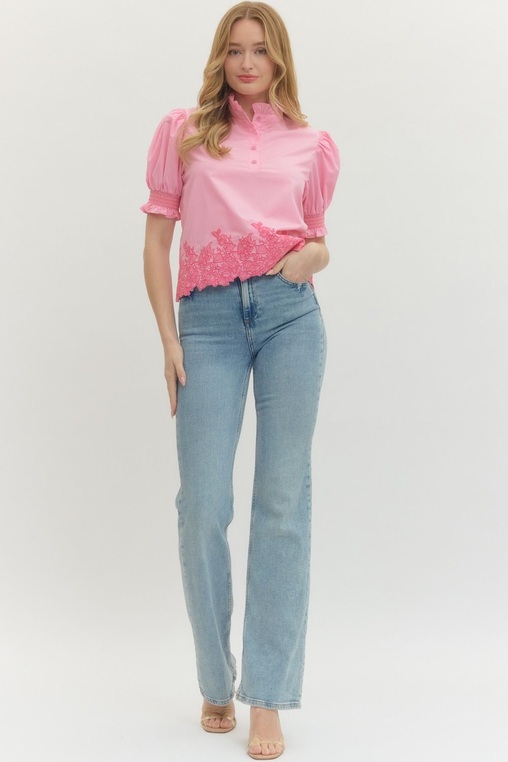 Woman wearing a pink blouse with floral embroidery and blue jeans on a white background