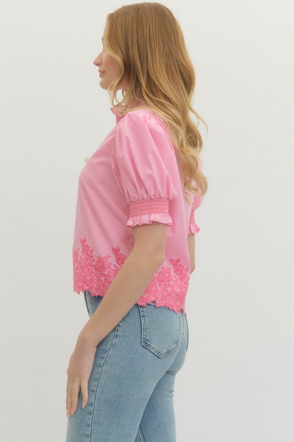 Woman wearing a pink blouse with lace details and blue jeans on a light gray background