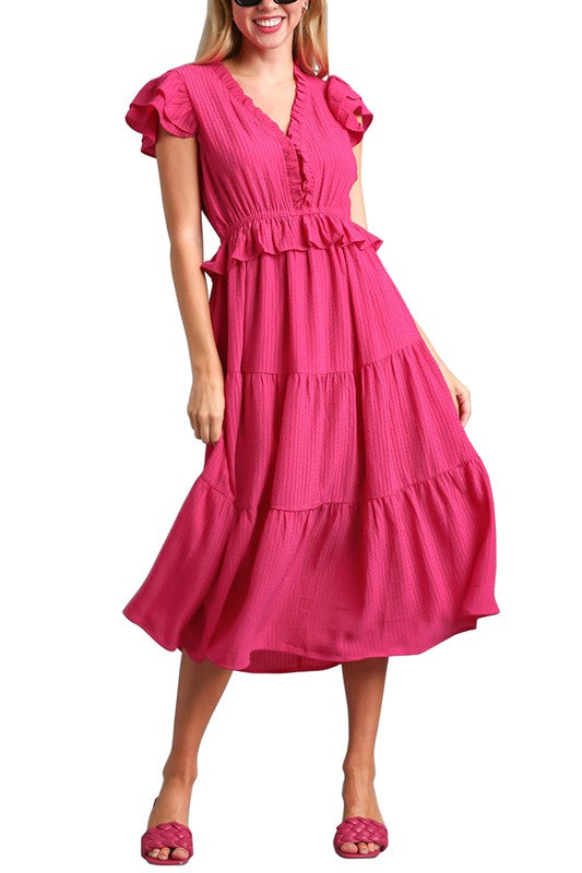 Model wearing The Pink Posh Midi Dress — a bright magenta tiered midi dress with ruffle sleeves, v-neckline, and smocked waist detail.