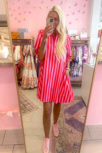 Woman taking a mirror selfie wearing a red and pink striped dress in a store.