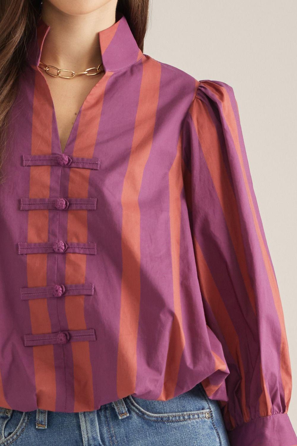 Close-up of plum and rust striped blouse showing stand collar, fabric-covered frog buttons and puff sleeve.