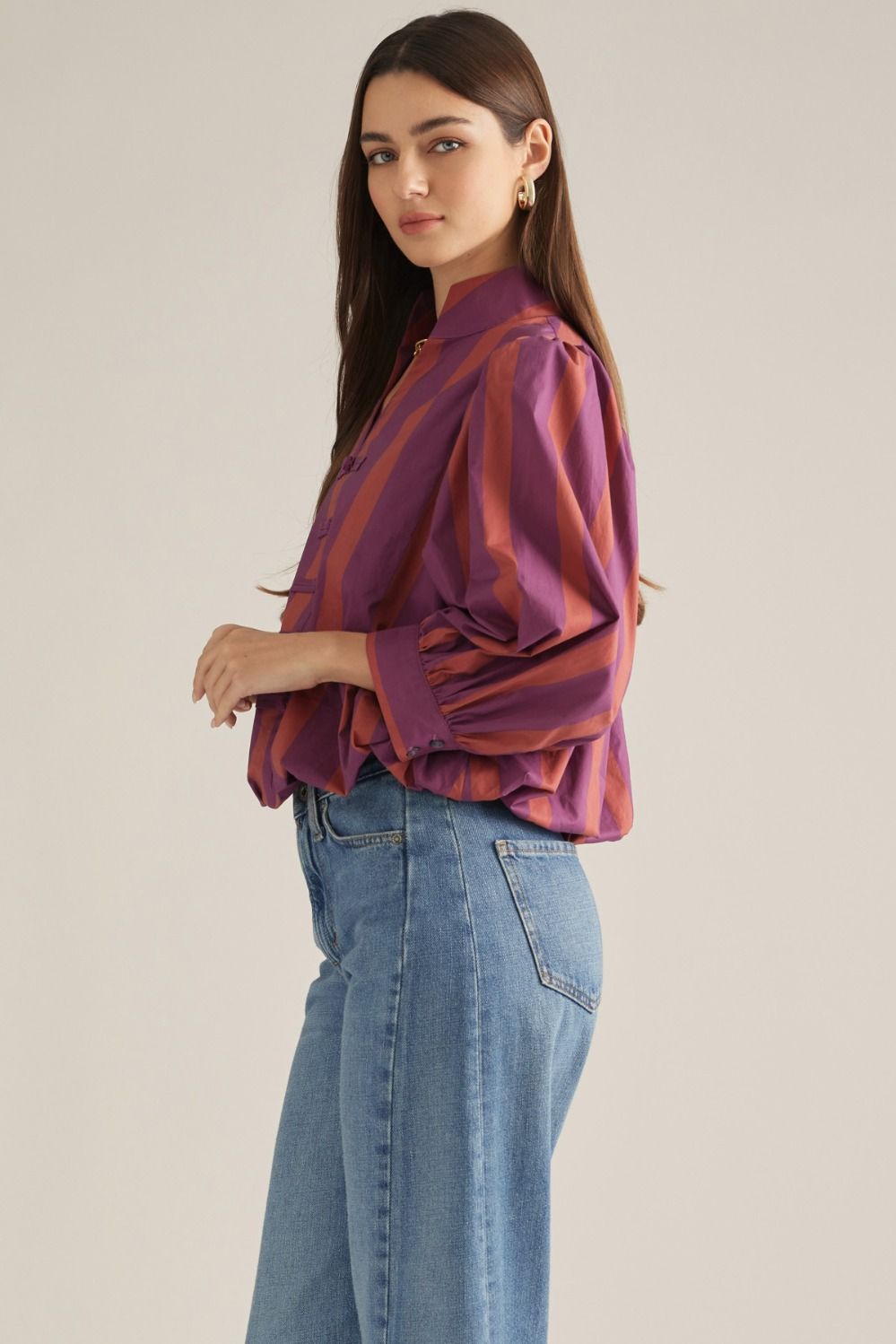 Side view of plum and rust striped blouse with voluminous puff sleeves styled with blue jeans.