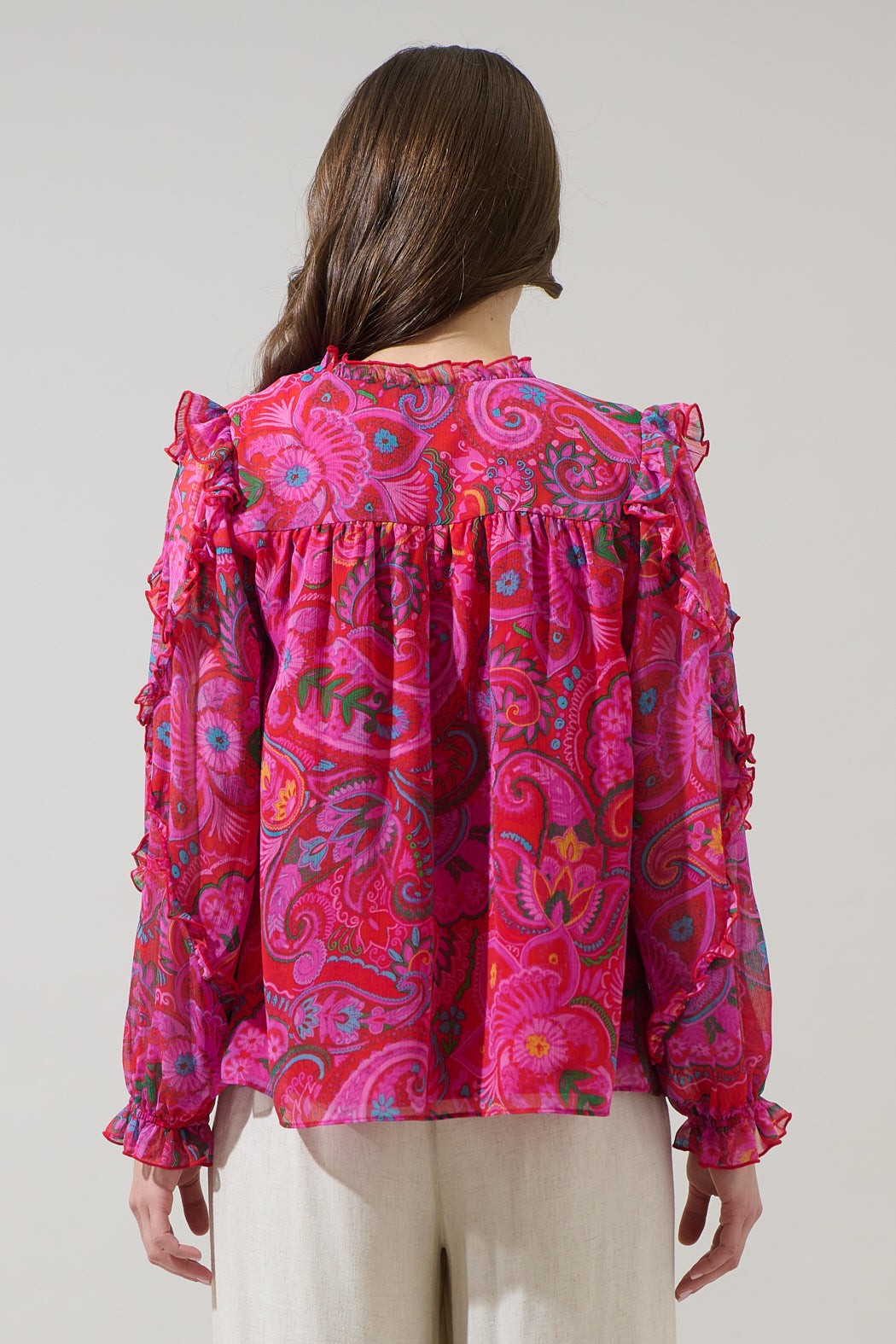 Woman wearing a vibrant pink paisley blouse against a plain background