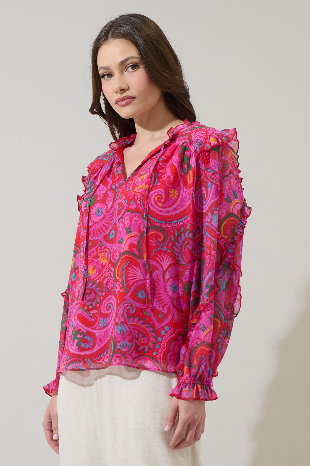 Woman wearing a vibrant pink paisley blouse against a plain background