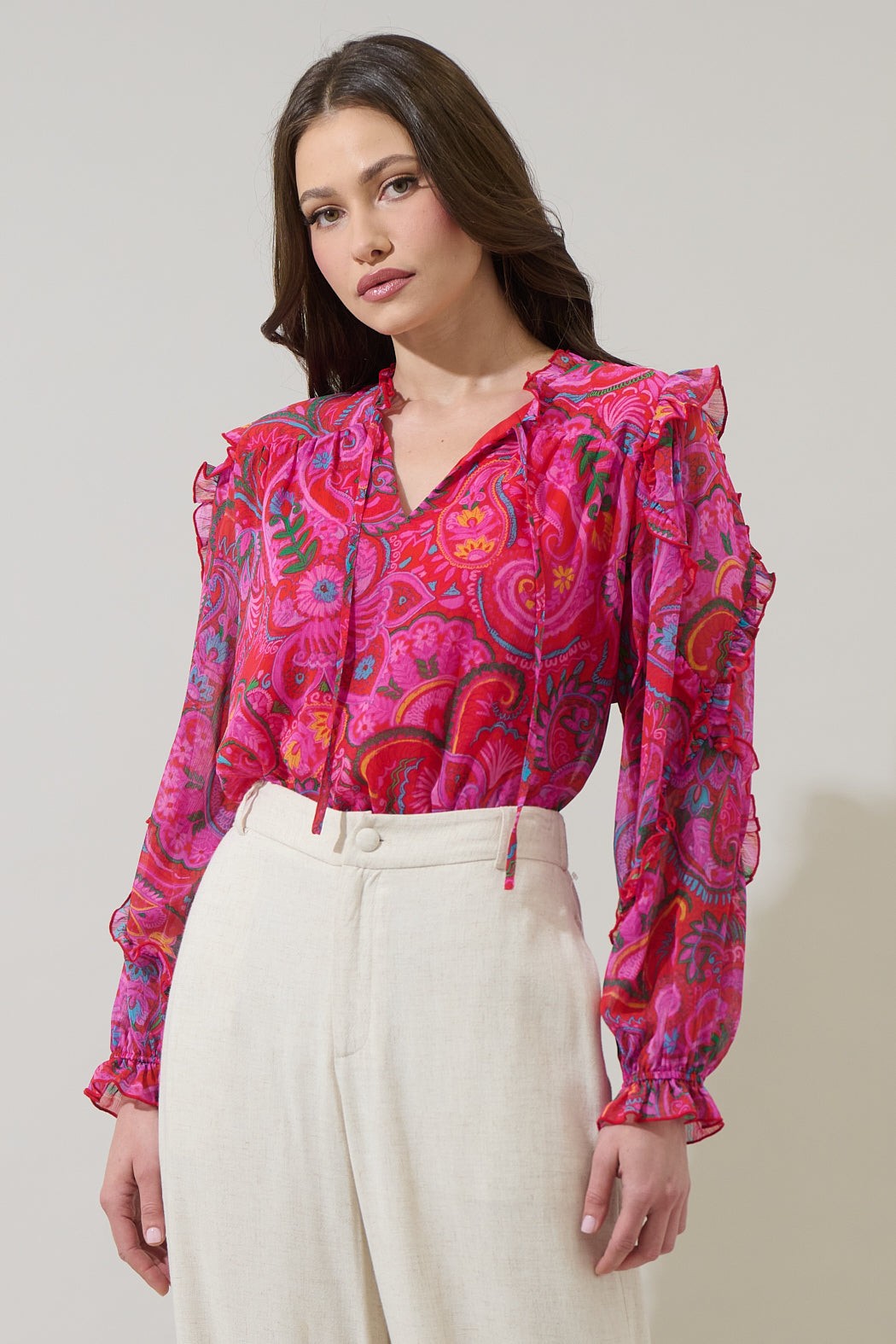 Woman wearing a vibrant pink patterned blouse with long sleeves against a plain background