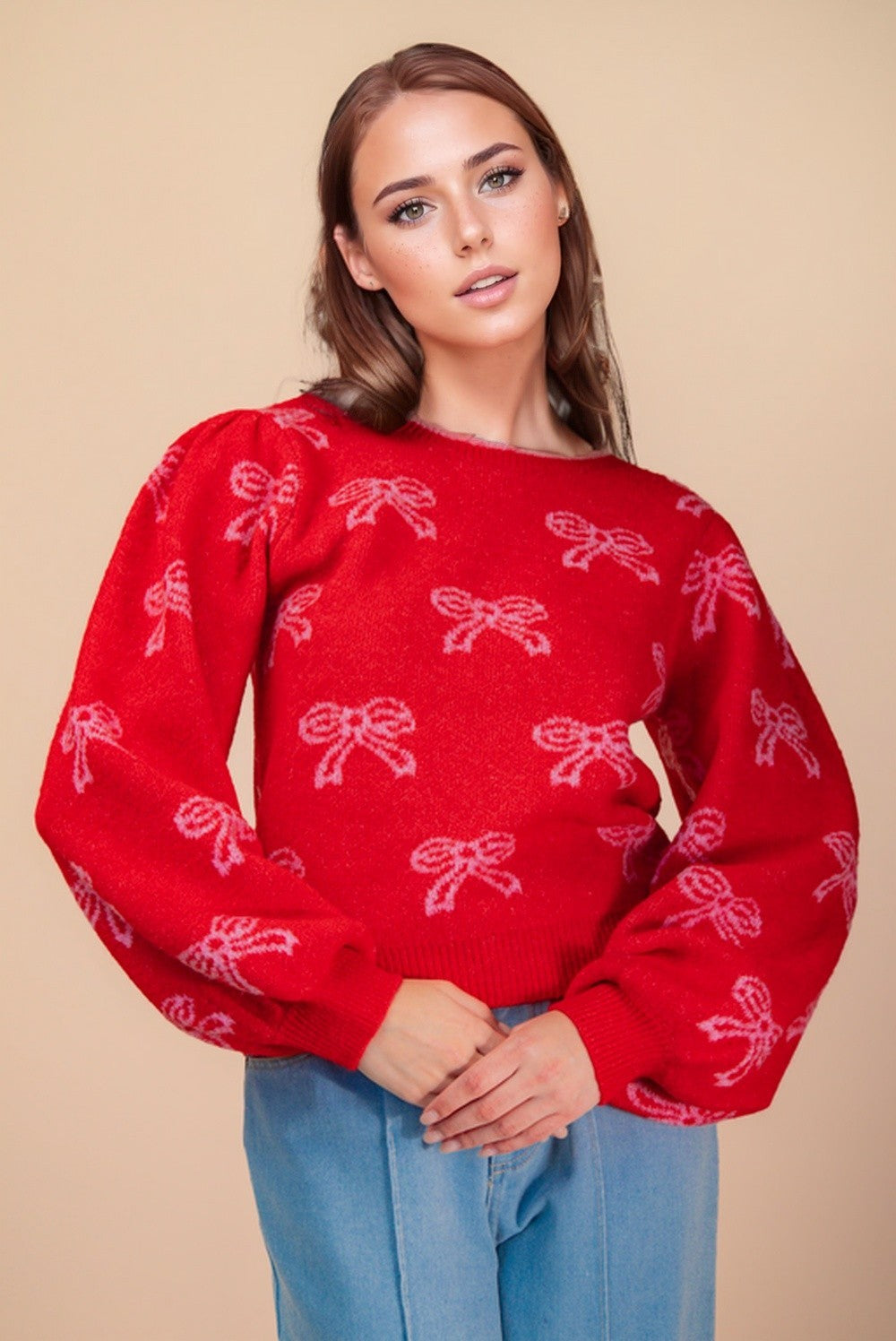 Model wearing a red puff sleeve sweater with pink bow pattern — The Merry Bow Knit holiday sweater from Milo & Lily Boutique.
