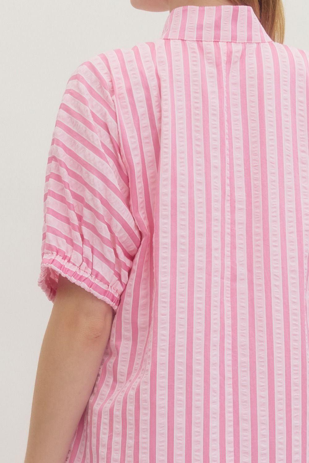 Pink and white striped shirt worn by a person on a plain background