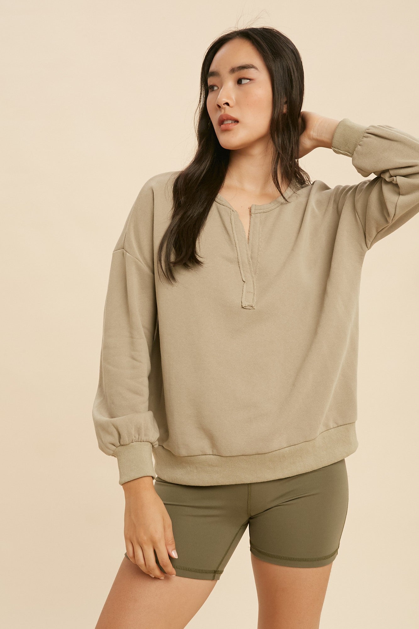 Woman wearing a beige sweatshirt and green shorts against a beige background