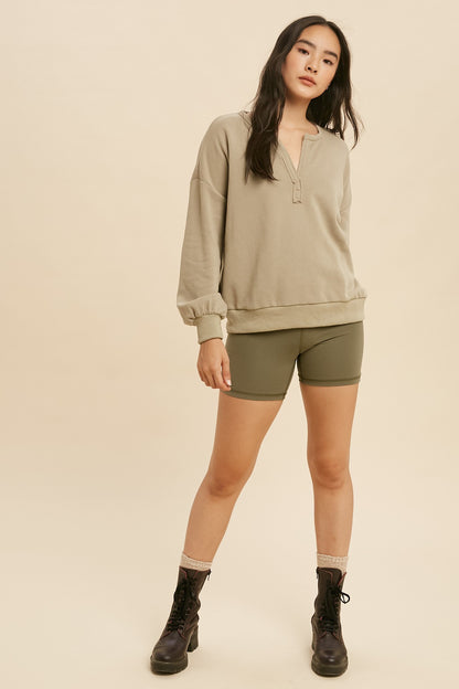 Woman wearing a beige long-sleeve shirt and green shorts on a beige background
