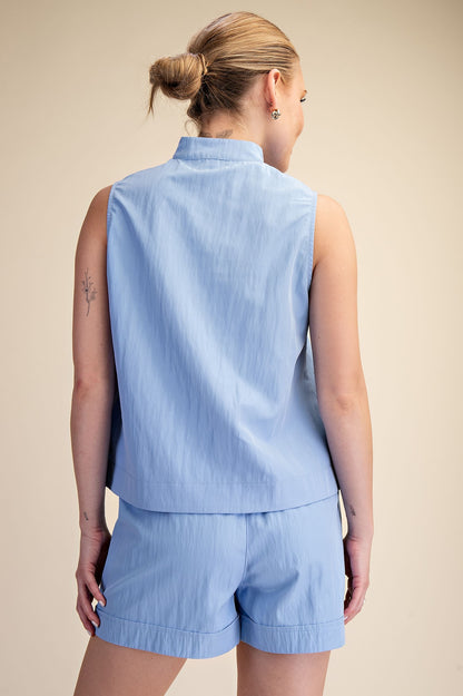 Woman wearing a light blue sleeveless top and shorts set against a beige background