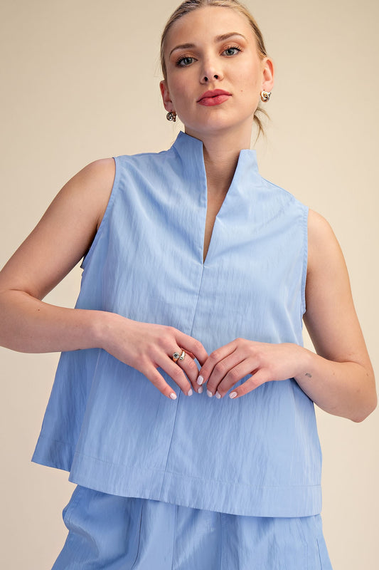 Woman wearing a light blue sleeveless top with a plain background