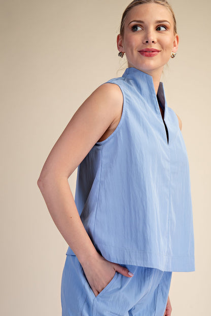 Woman wearing a light blue sleeveless top and pants against a beige background